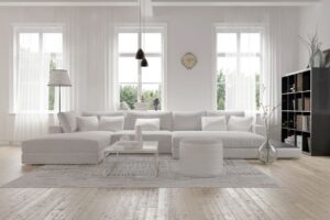 A living room with a white sectional and white sheer curtains on the windows